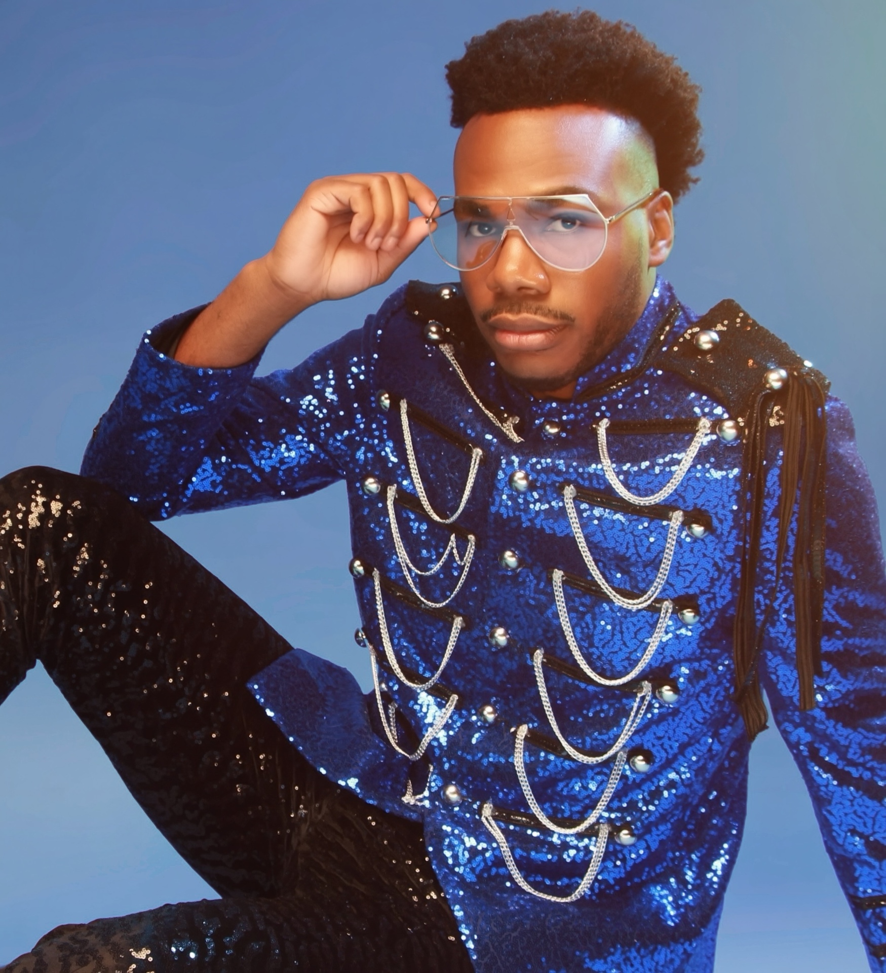 Jerry Stacks in a blue sequined military-style jacket with chains, adjusting his glasses